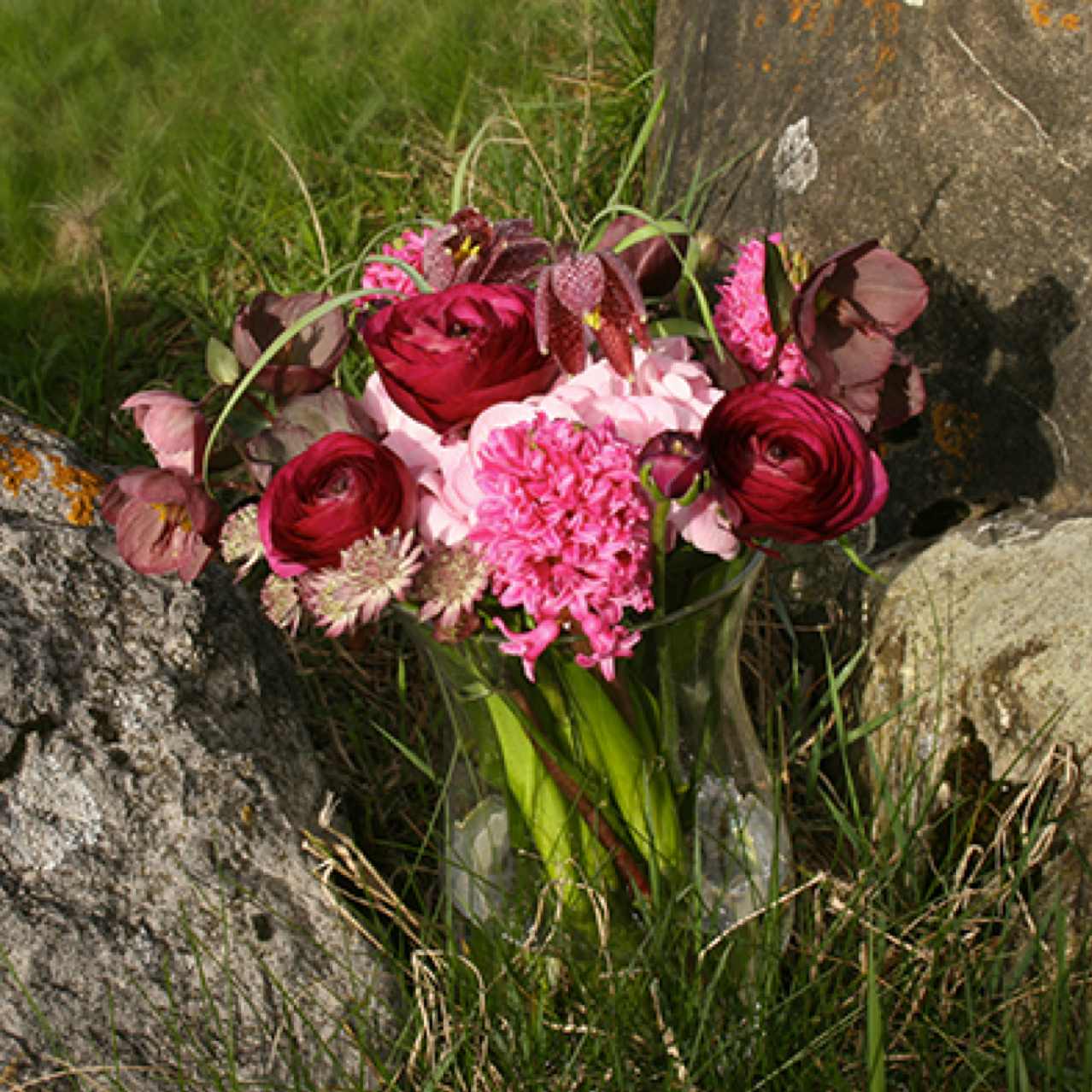 Arrangement de fleurs coupées pastel dans un vase transparent. Avec des Renoncules, Jacinthes, Hortensia, Hellebores, Astrancia et Fritillaire.