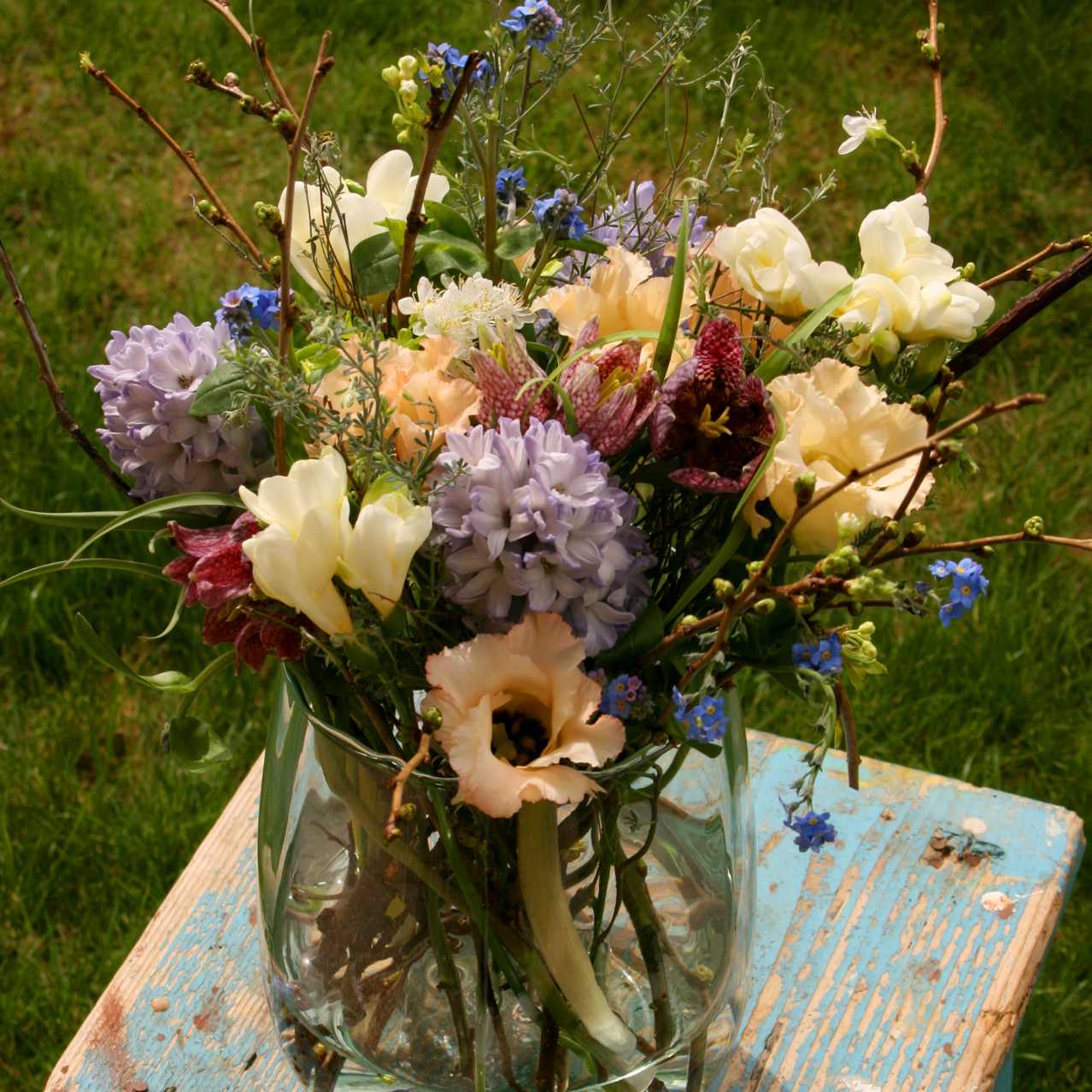 Arrangement de fleurs coupées pastel dans un vase en verre. Avec des Jacinthes, Lysianthus, Myosotis, Freesia et Fritillaires.