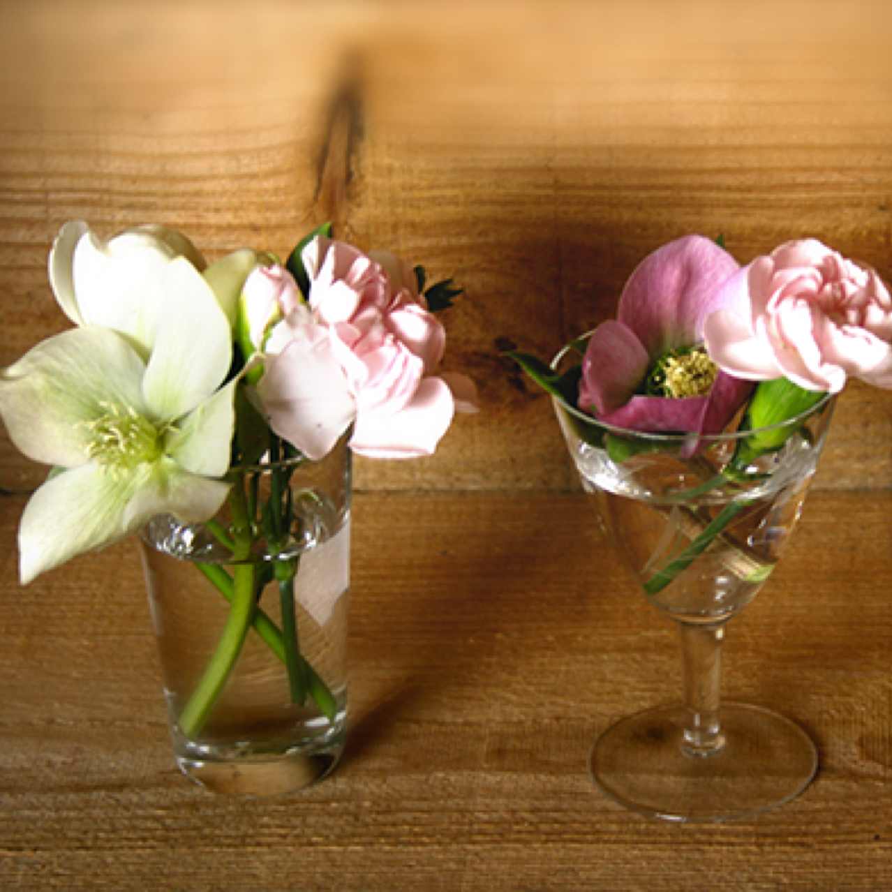 Trois petits arrangements de fleurs coupées dans des verres à vins. Avec Fressia, Œillet et Hellebore. 